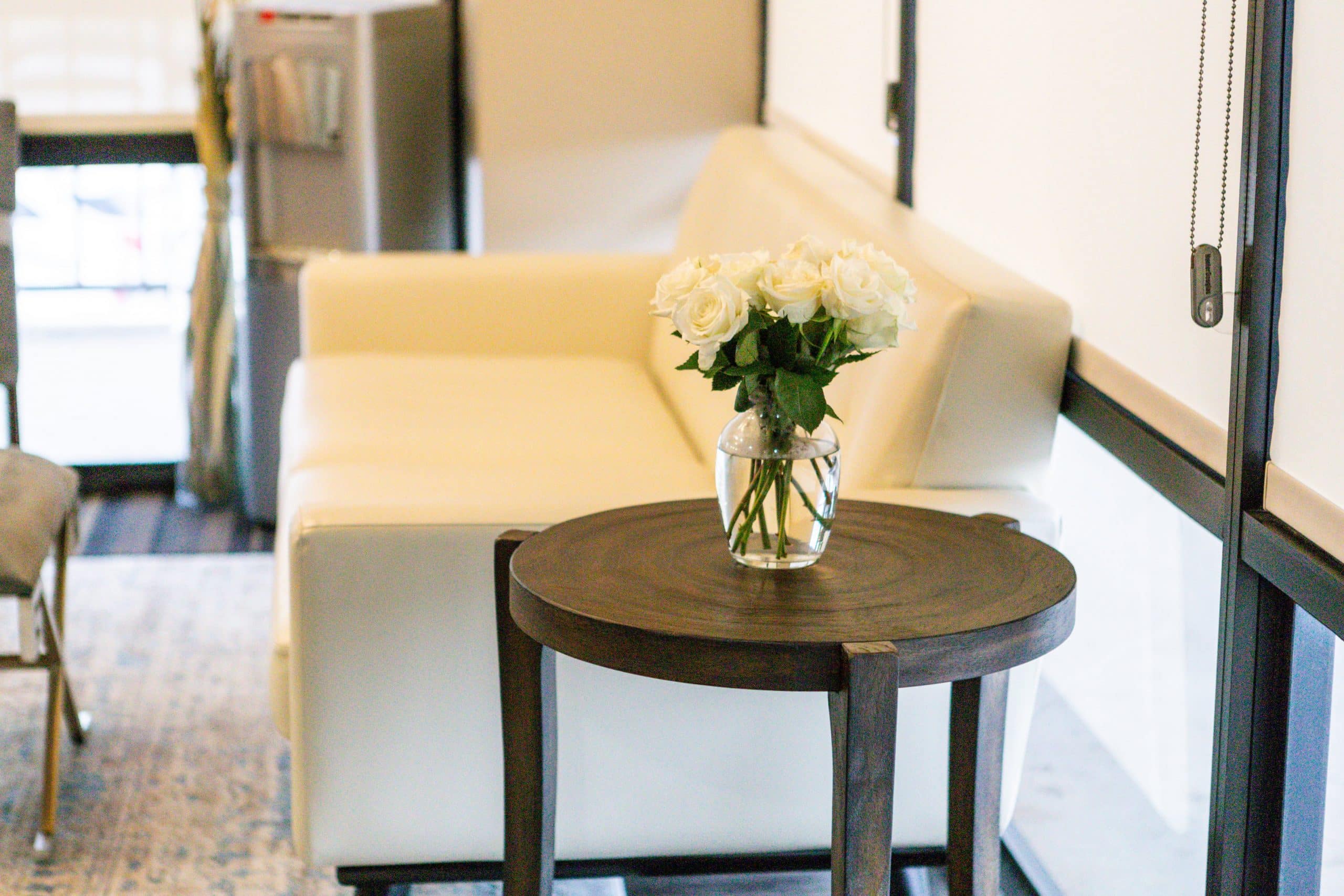 Modern dental office waiting room with cream chair and side table holding white flowers.