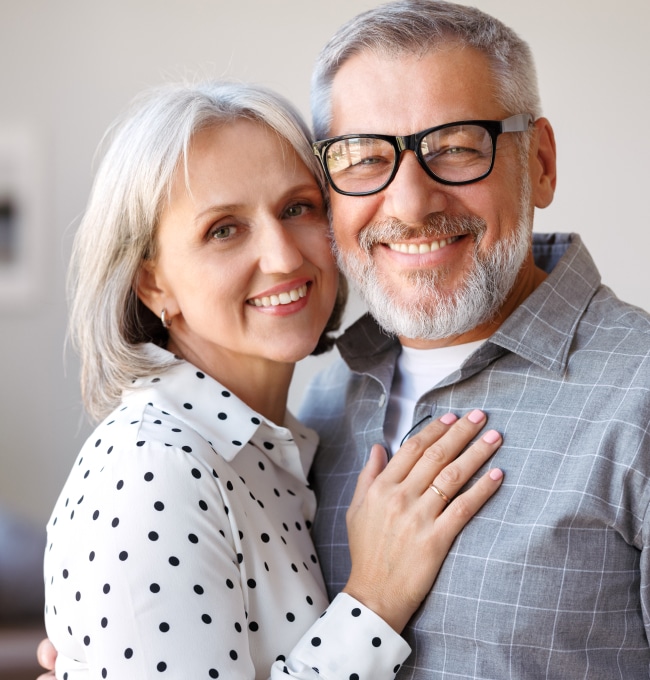 Middle-aged couple smiling together in casual clothing, professional portrait setting for dental practice.