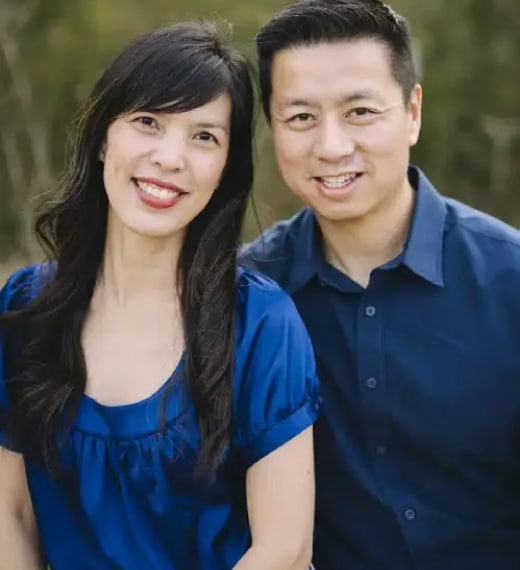 Two smiling dental professionals in blue attire posed outdoors against a green background.