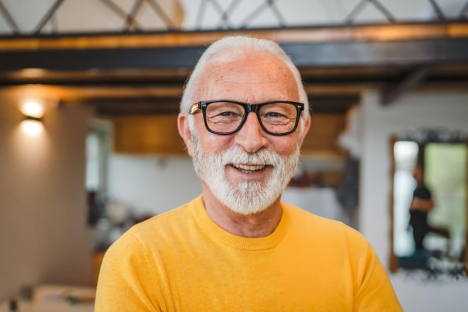 Smiling older man with glasses wearing yellow shirt in modern dental office interior