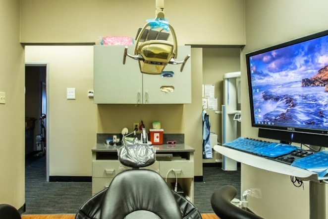 Patient in dental chair facing overhead light and monitor in modern dentistry office treatment room.