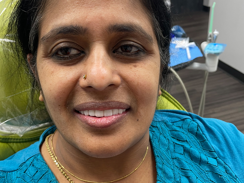 Woman smiling at camera in dental office wearing blue shirt and gold necklace.