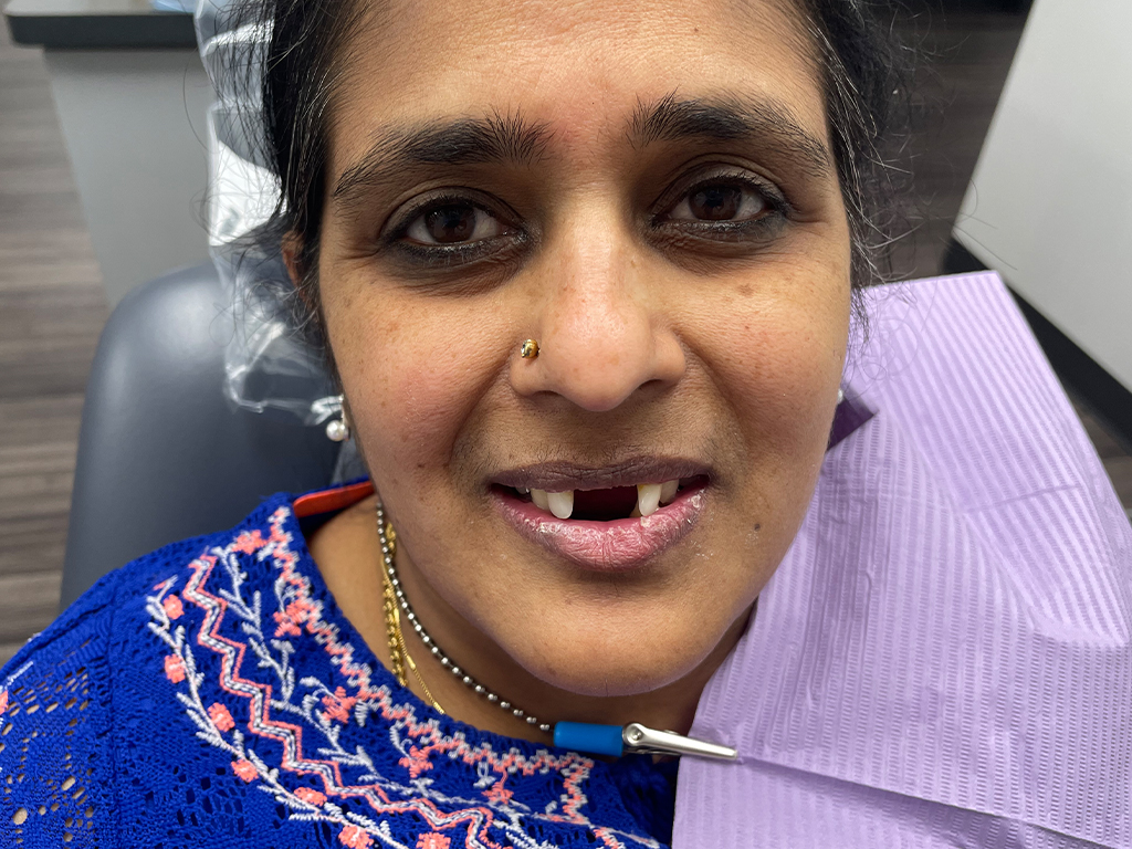 Woman smiling at camera in dental office setting wearing blue and purple clothing.
