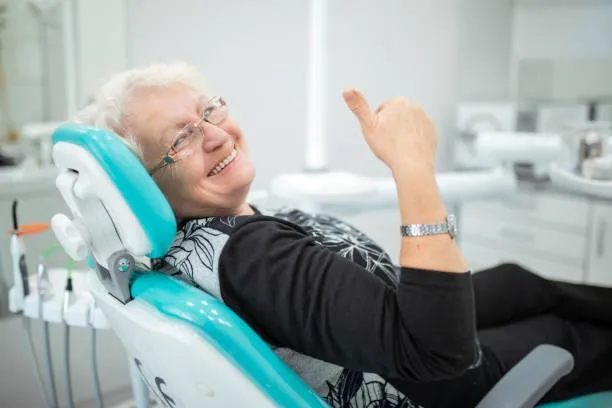 Elderly patient smiling in dental chair at Denton Smiles Dentistry office during examination.