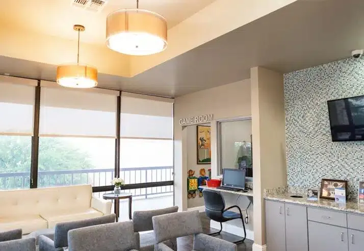 Modern dental office waiting room with comfortable seating, large windows, and contemporary lighting fixtures.