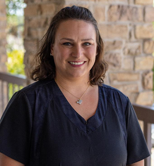 Professional woman smiling at camera wearing dark scrubs against brick wall background.