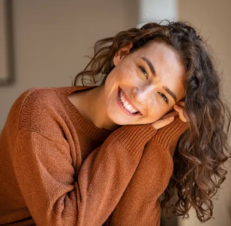 Woman in rust sweater smiling warmly indoors, professional headshot for dental practice.