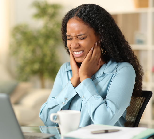 Woman smiling during video call at desk with laptop and coffee cup in bright office.