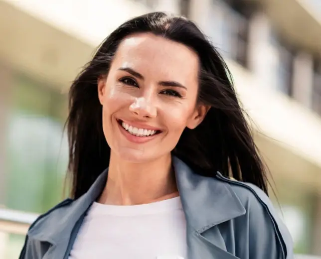 Smiling woman wearing blue jacket outdoors in front of blurred building background