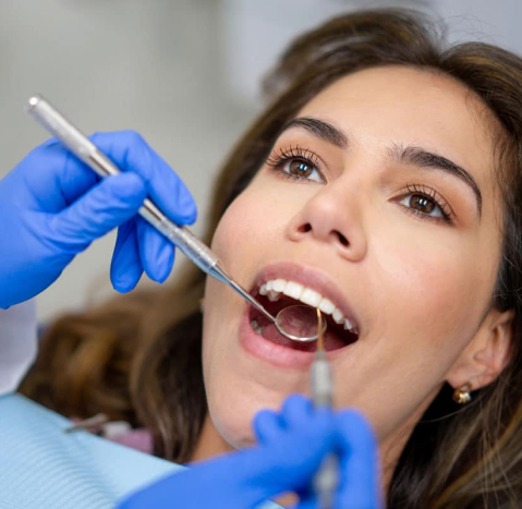 Dentist in blue gloves examining patient's teeth during dental checkup appointment.