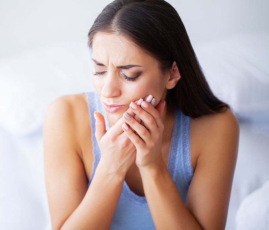 Woman holding cheeks in pain, experiencing dental discomfort or toothache indoors.