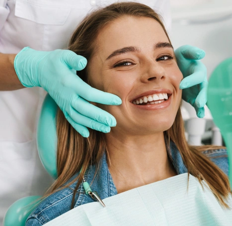 Young woman smiling at dental checkup with dentist wearing gloves in clinical setting.
