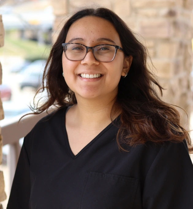 Woman wearing glasses and black shirt smiling at camera in dental office setting.
