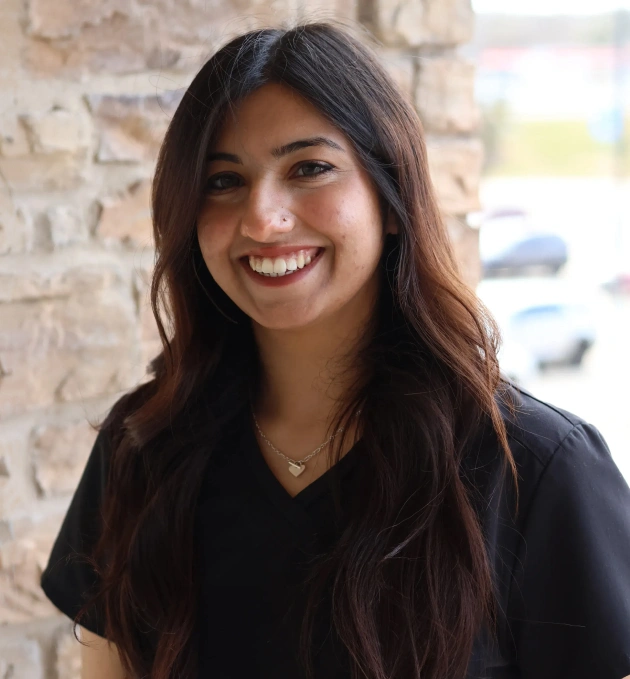 Young woman smiling at camera, professional headshot against brick wall background.