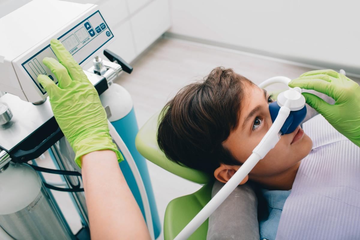 Young child receiving sedation dentistry treatment in dental chair with protective eyewear.
